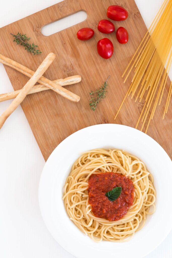 white ceramic bowl with pasta and red tomato on brown wooden table