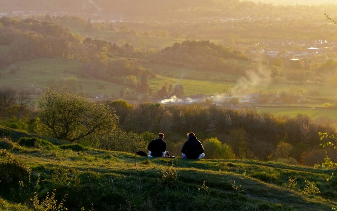 Two people sit on a hill at sunset.