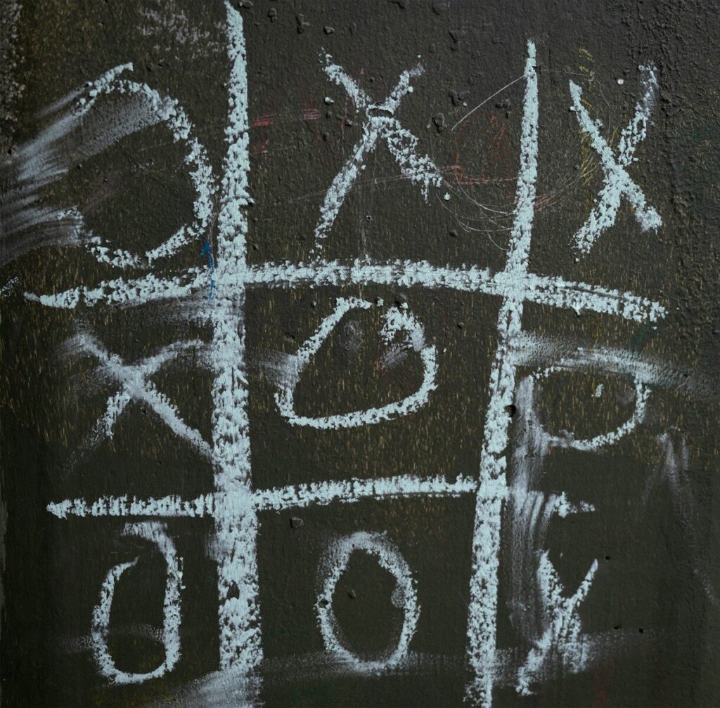A chalk-drawn tic-tac-toe game on a dark surface